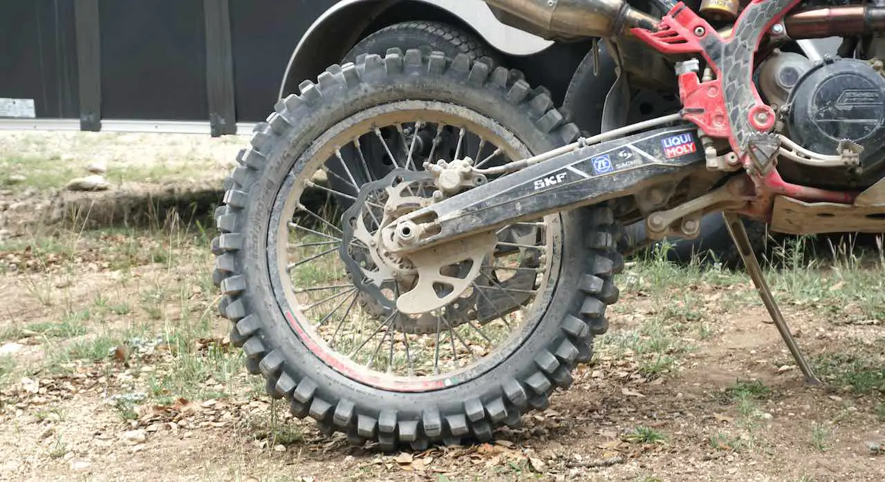 A dusty rear wheel of a dirt bike with a brake disc cover