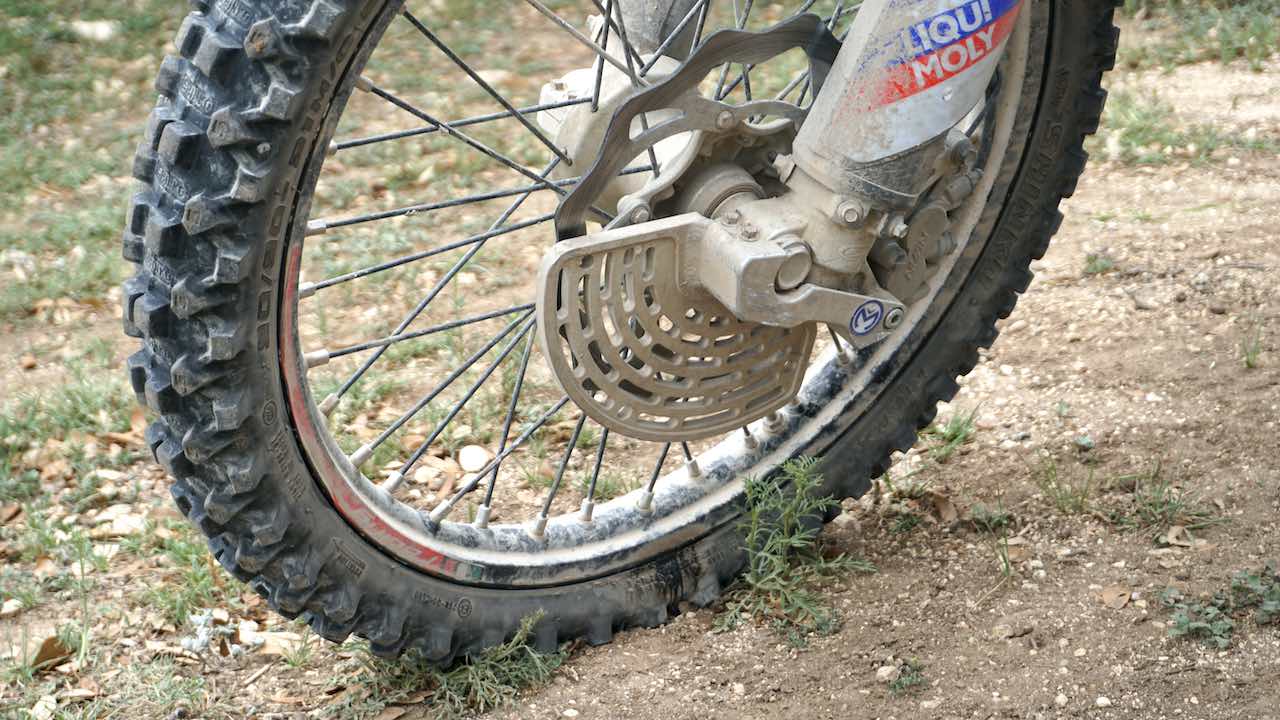 A dusty front wheel of a dirt bike with a disc brake guard