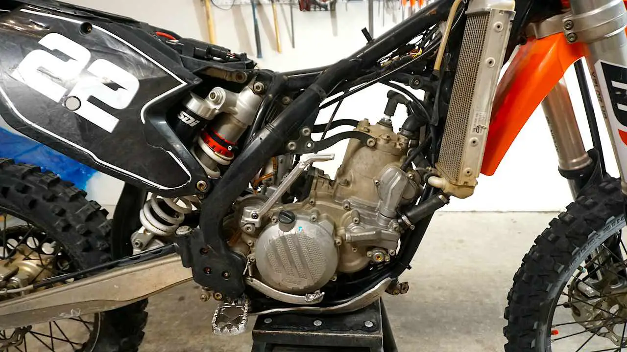 A dirt bike standing on a center stand with the seat, gas tank and plastics removed