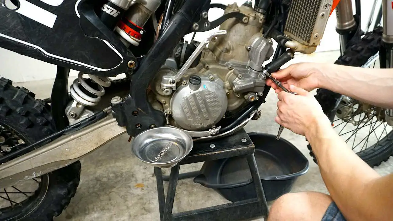 Hands holding a socket wrench and opening the right side radiator hose clamp on a dirt bike