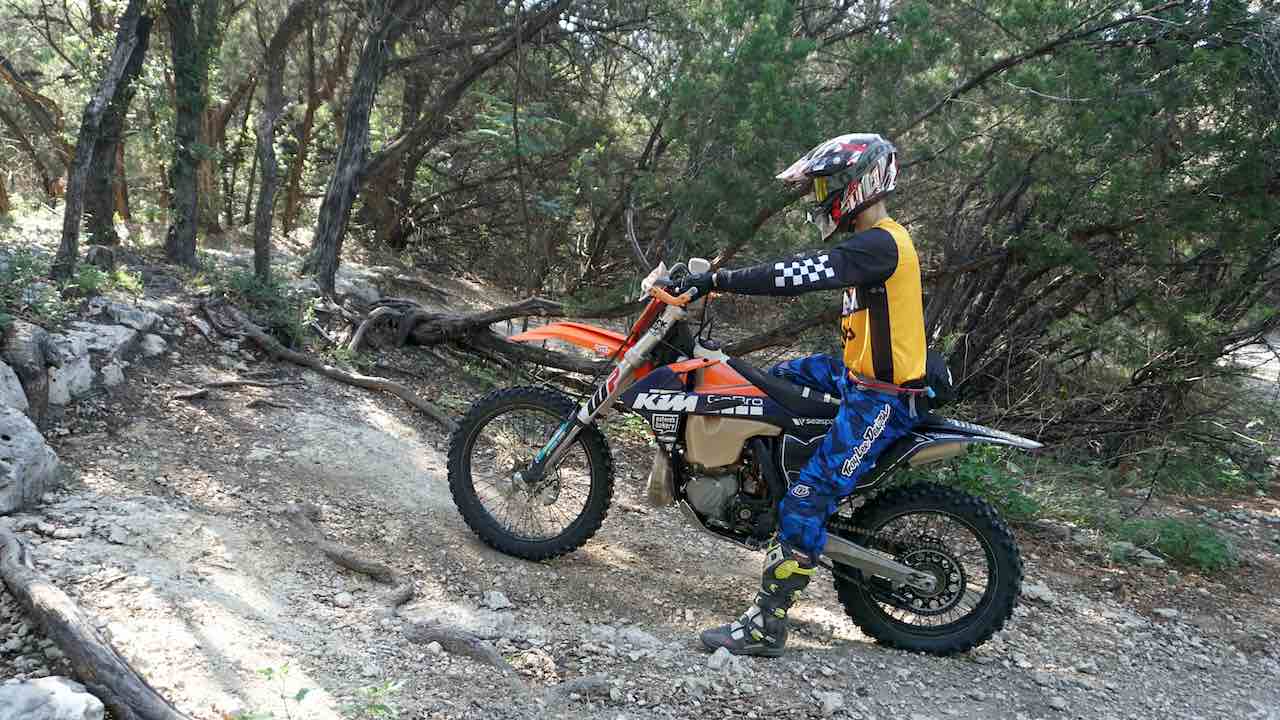 Dirt bike on an incline with a person sitting on the back of the seat