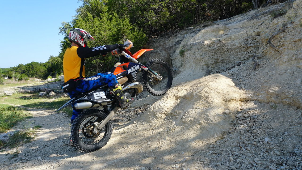 Rider with a dirt bike using the clutch to lift front end up to a wheelie