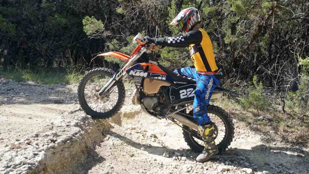 Dirt bike front tire in a sand stone ledge with rider sitting on the back of the seat and left leg down