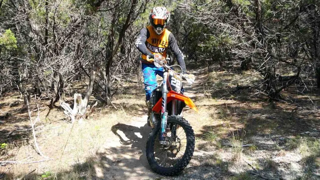 Person static balancing with a dirt bike on a single track trail in the woods