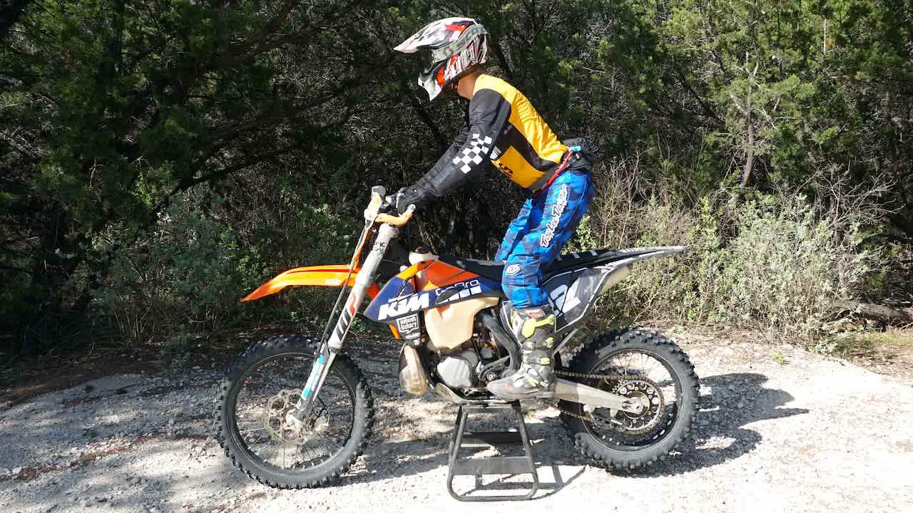Person standing on a dirt bike placed on a center stand in a neutral riding position