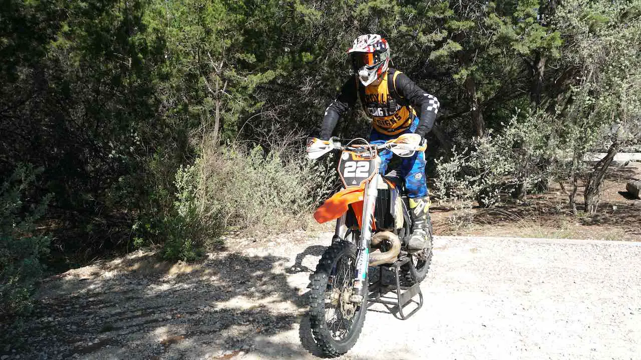 Person standing on a dirt bike looking ahead and balancing on the foot pegs
