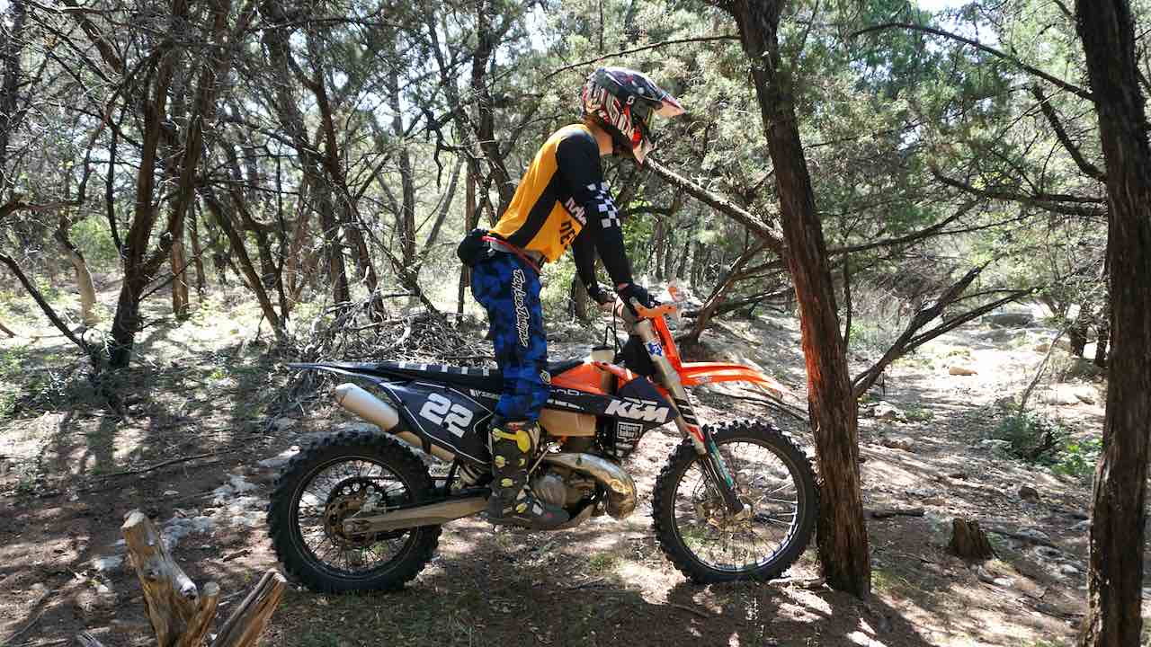 Dirt bike pushing against a tree with a rider standing on foot pegs
