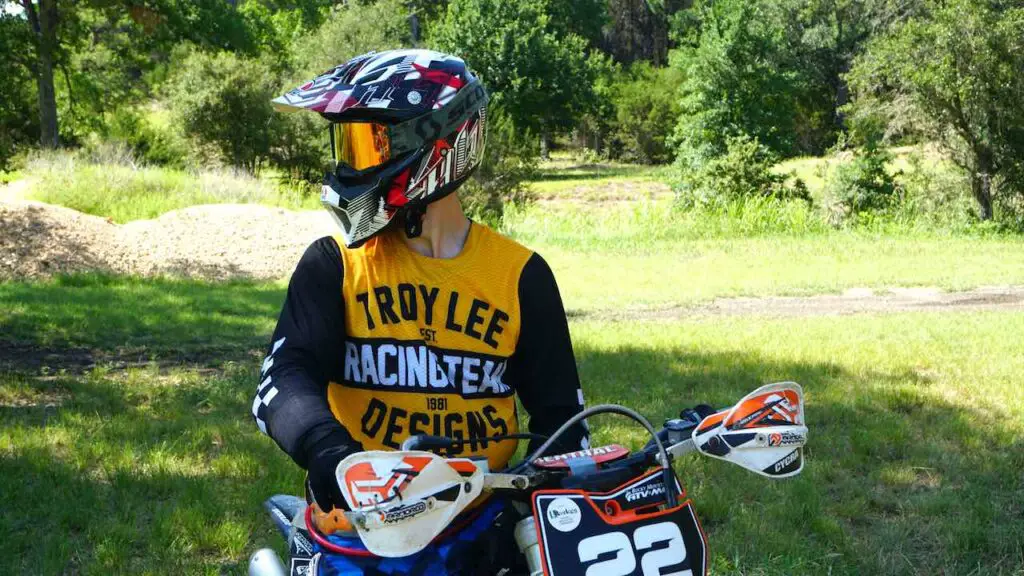 Rider with dirt bike gear on looking back while sitting on a dirt bike on a grassy field