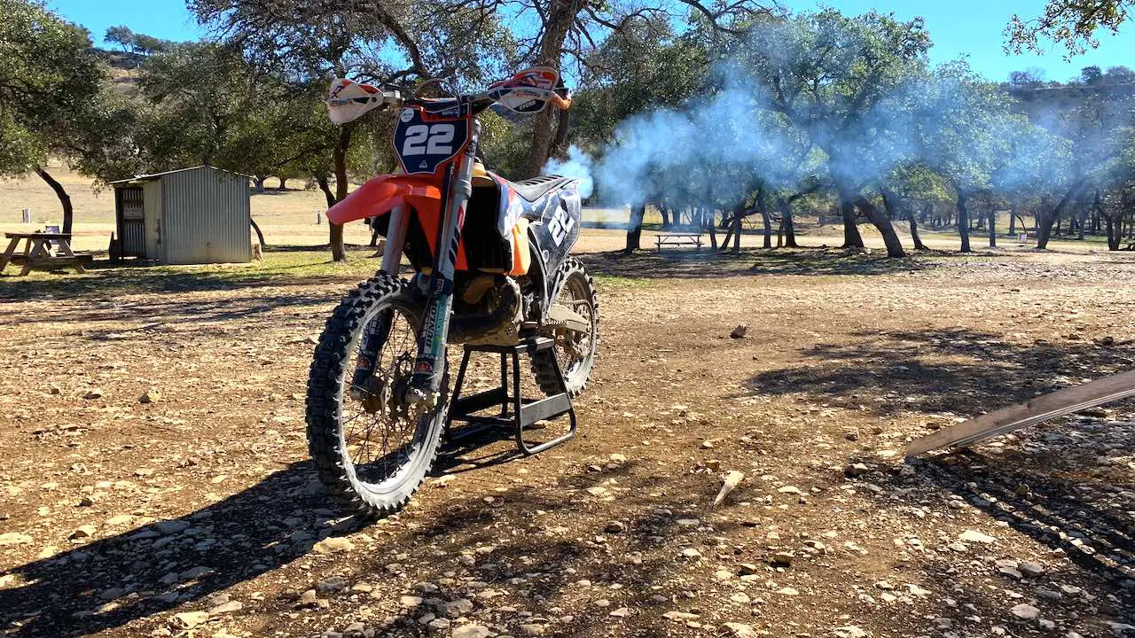 A 2-stroke dirt bike on a center stand idling and smoking 2-stroke oil