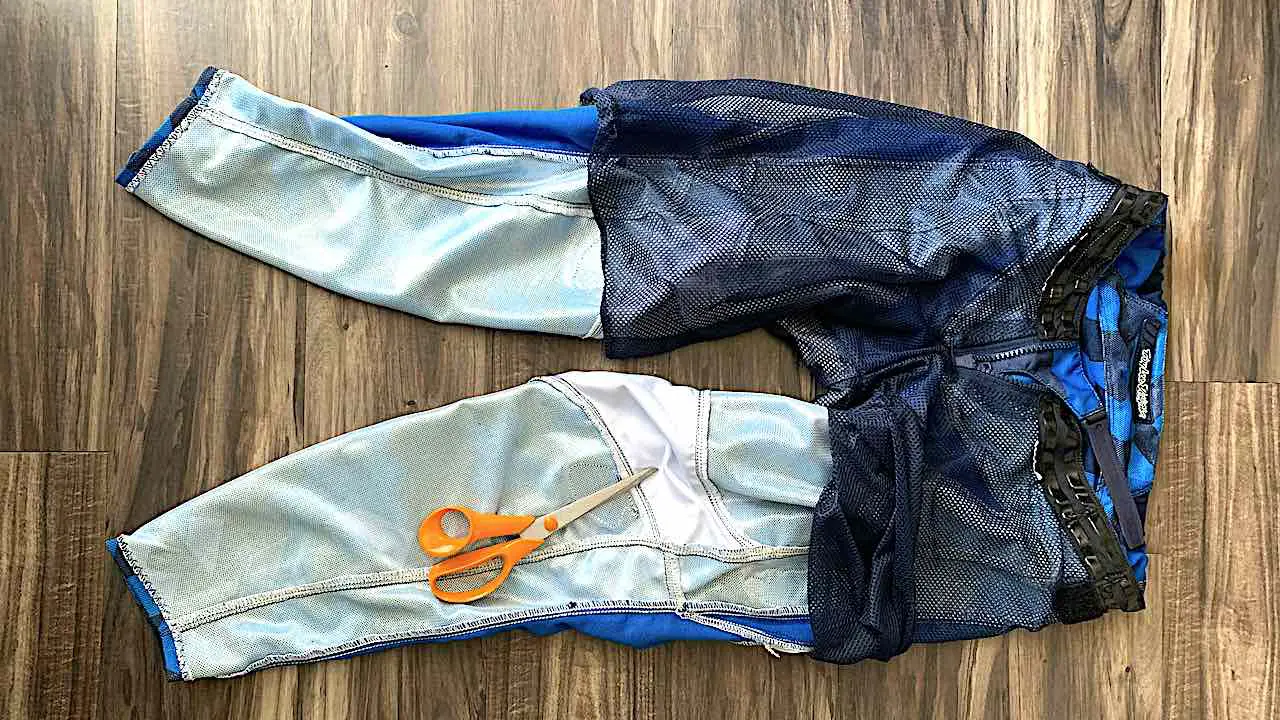 Cutting dirt bike pants for hot weather by removing the mesh material inside the pants with scissors