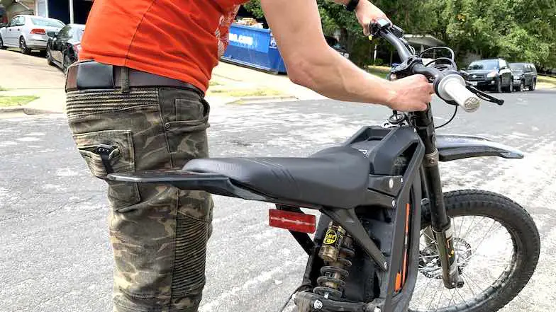 Rider adjusting front suspension clickers on an electric dirt bike