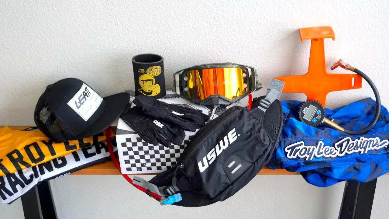 Dirt bike gifts, such as goggles, riding jerseys, and hydration pack, laid on top of a bench