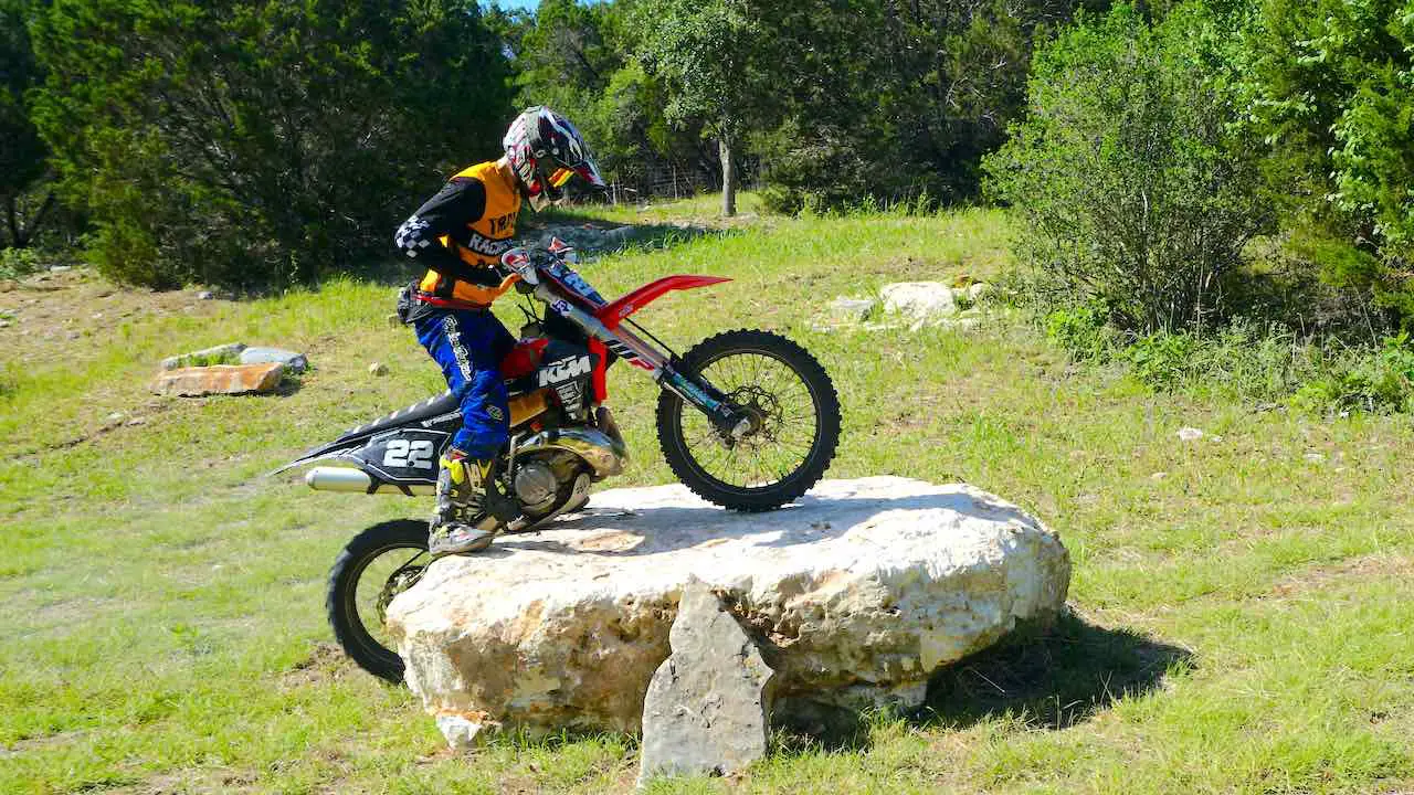 A dirt biker going over a boulder while a dirt bike skid plate is protecting the engine and frame on a KTM XCW300