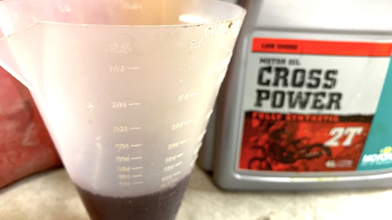 2 stroke oil measuring cup with 2 stroke oil in front of a 2 stroke oil container
