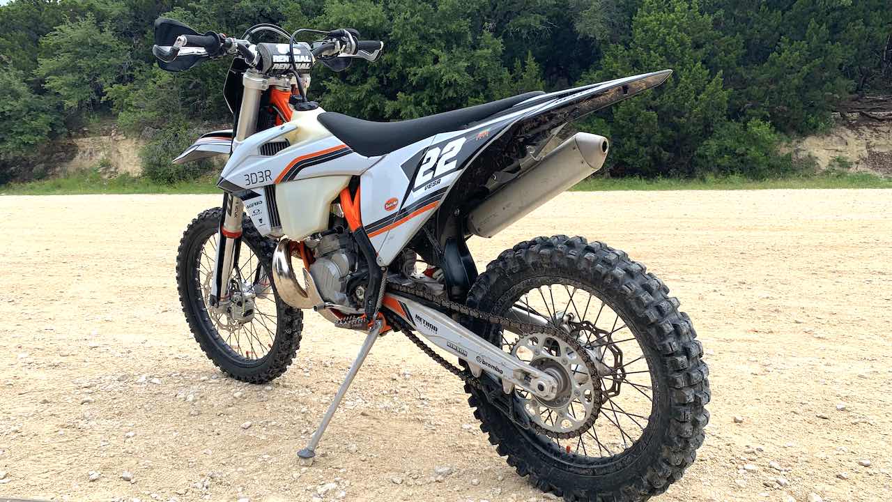 The 2023 KTM XCW 300 on a sandy parking lot ready to ride.